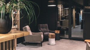 A modern interior with a grey armchair, a wooden side table, and a potted plant. - Hotel Majer'ca (Bohinj)