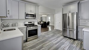 A modern kitchen with white cabinetry, stainless steel appliances, and a wood-patterned floor. - LOCATION,PRACTICALITY AND COMFORT MEET! BEACH BLOCK! BRING YOUR EXTENDED FAMILY! (Atlantic City)