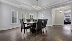 A dining room with a dark wood table and chairs, a chandelier, and large windows with shutters. - LOCATION,PRACTICALITY AND COMFORT MEET! BEACH BLOCK! BRING YOUR EXTENDED FAMILY! (Atlantic City)