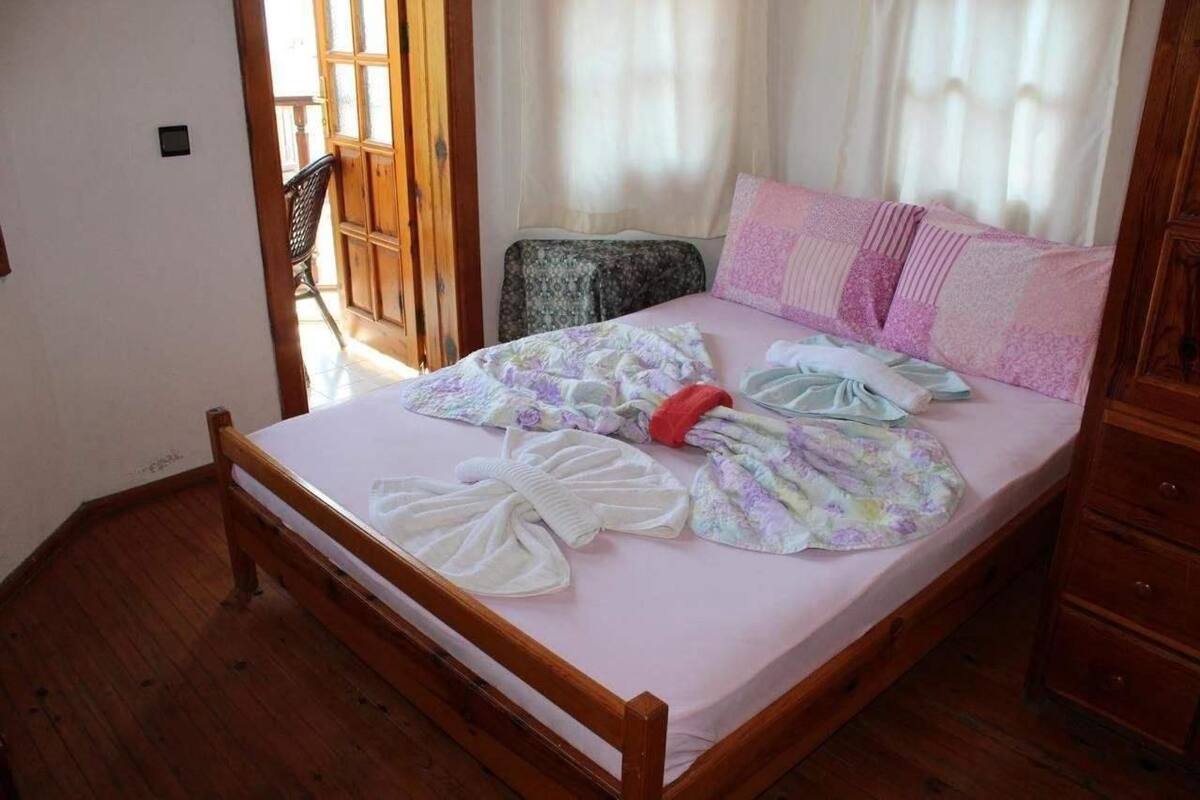Una cama bien hecha con edredón floral, almohadas rosa y blancas y un cabecero de madera.