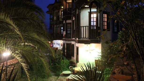 A multi-story building with balconies, a well-lit entrance, and a garden area with palm trees. - Orkide Apart Hotel (Ula)