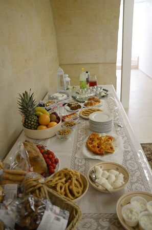 Une table dressée avec divers aliments, notamment des fruits, du pain, des pâtisseries et des condiments.