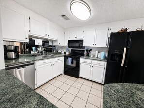 A kitchen with white cabinets, a black refrigerator, a stove, and a microwave. - Sugartop Resort 6th-Floor Corner Condo: Breathtaking Mountain Views - 2BR (Sugar Mountain)
