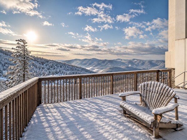 A snow-covered deck with a wooden chair and a view of snow-covered mountains.