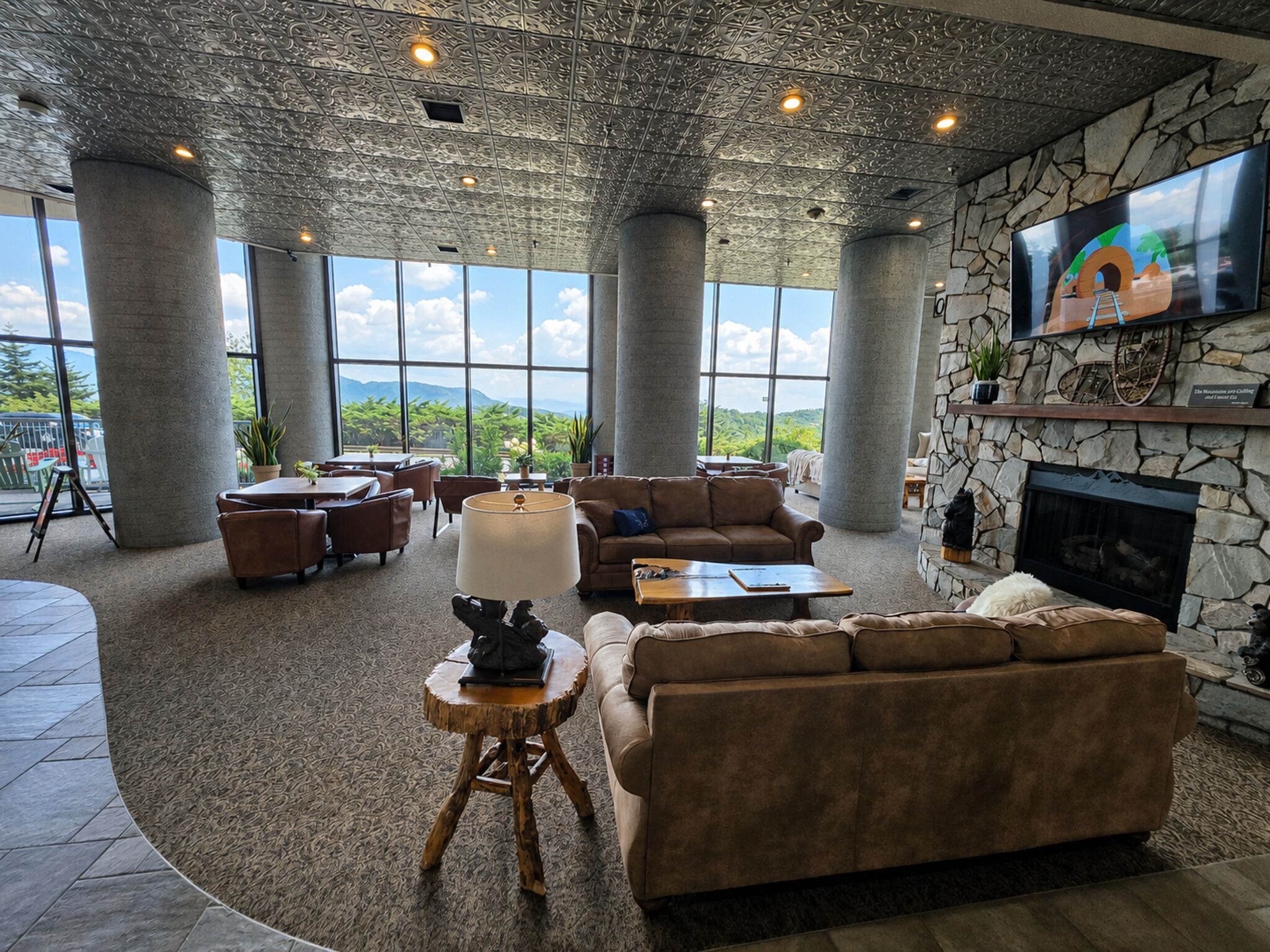 A spacious lounge with a stone fireplace, comfortable seating, and large windows offering a view of the outdoors.