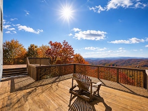 Une terrasse en bois offrant une vue sur le feuillage automnal et les montagnes lointaines.