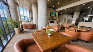 A spacious indoor area with a large wooden table surrounded by leather chairs, a stone wall with a television, and a view through large windows. - Sugartop Resort 6th-Floor Corner Condo: Breathtaking Mountain Views - 2BR (Sugar Mountain)