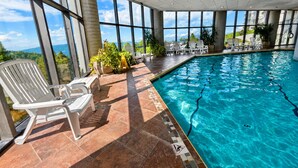 An indoor swimming pool with clear blue water, surrounded by large windows offering a view of the outdoors. - Sugartop Resort 6th-Floor Corner Condo: Breathtaking Mountain Views - 2BR (Sugar Mountain)