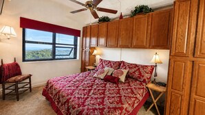 A bedroom with a large bed, wooden cabinets, a ceiling fan, and a window with a view. - Sugartop Resort 6th-Floor Corner Condo: Breathtaking Mountain Views - 2BR (Sugar Mountain)