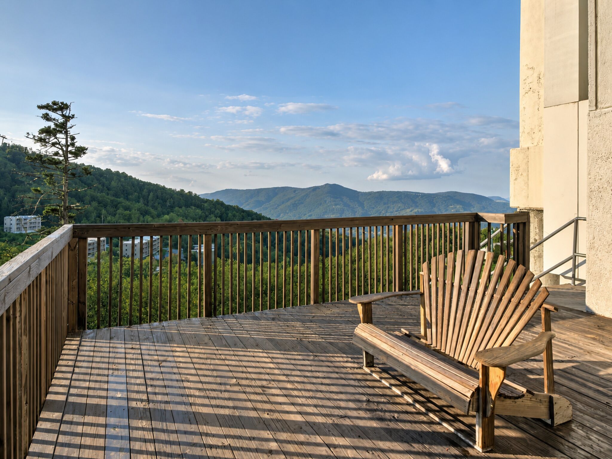 A wooden deck with a wooden chair and a railing overlooking a mountainous landscape.