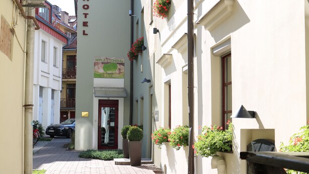 A narrow street with a hotel named "HOTEL" on the left, featuring a signboard and a red door. - Apple Economy Hotel (Kaunas)