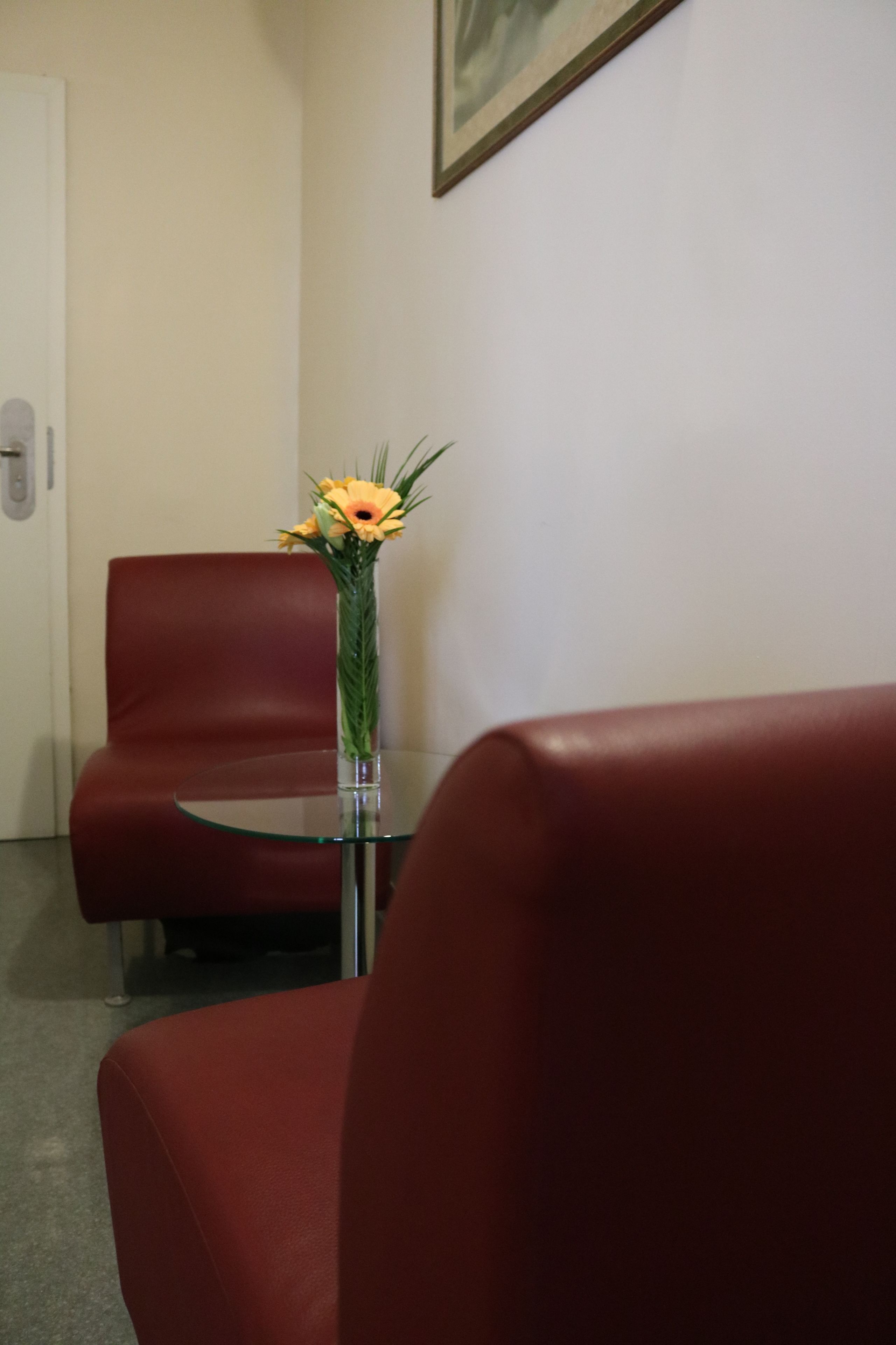 Een kamer met een glazen tafel, een bloemenvaas en rode leren stoelen.