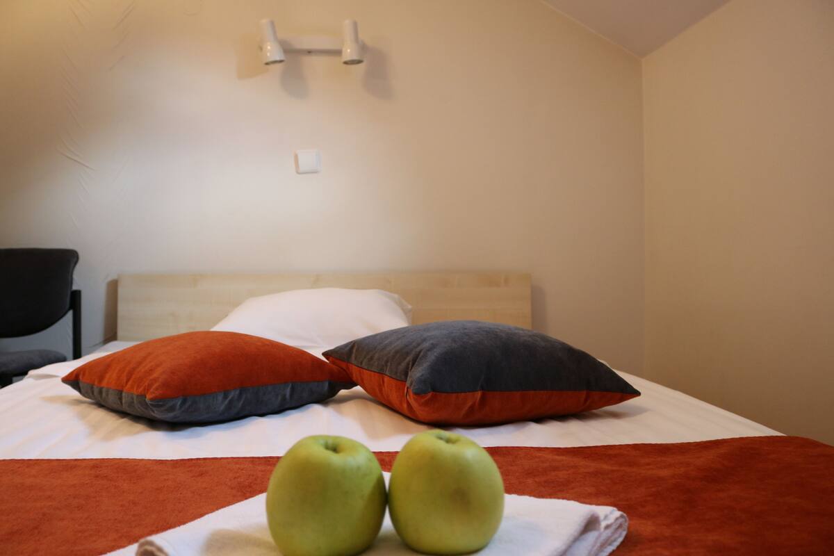 A neatly made bed with two pillows and two apples on a white blanket.