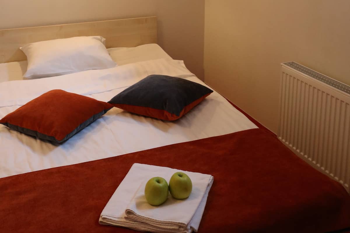 A hotel room with a bed, pillows, a red blanket, and two apples on a towel.