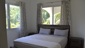 A bedroom with a large bed, two nightstands, a window with curtains, and a view of greenery outside. - THIS IS IT!!!!!! Newly built Renters Paradise (Sosua)