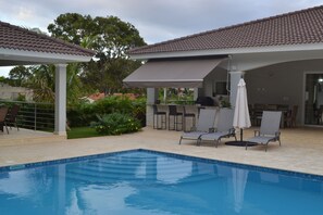 Une piscine avec des chaises longues et un espace patio couvert.