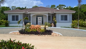 A two-story house with a tiled roof, a front entrance, and a landscaped garden with plants and a rock feature. - THIS IS IT!!!!!! Newly built Renters Paradise (Sosua)