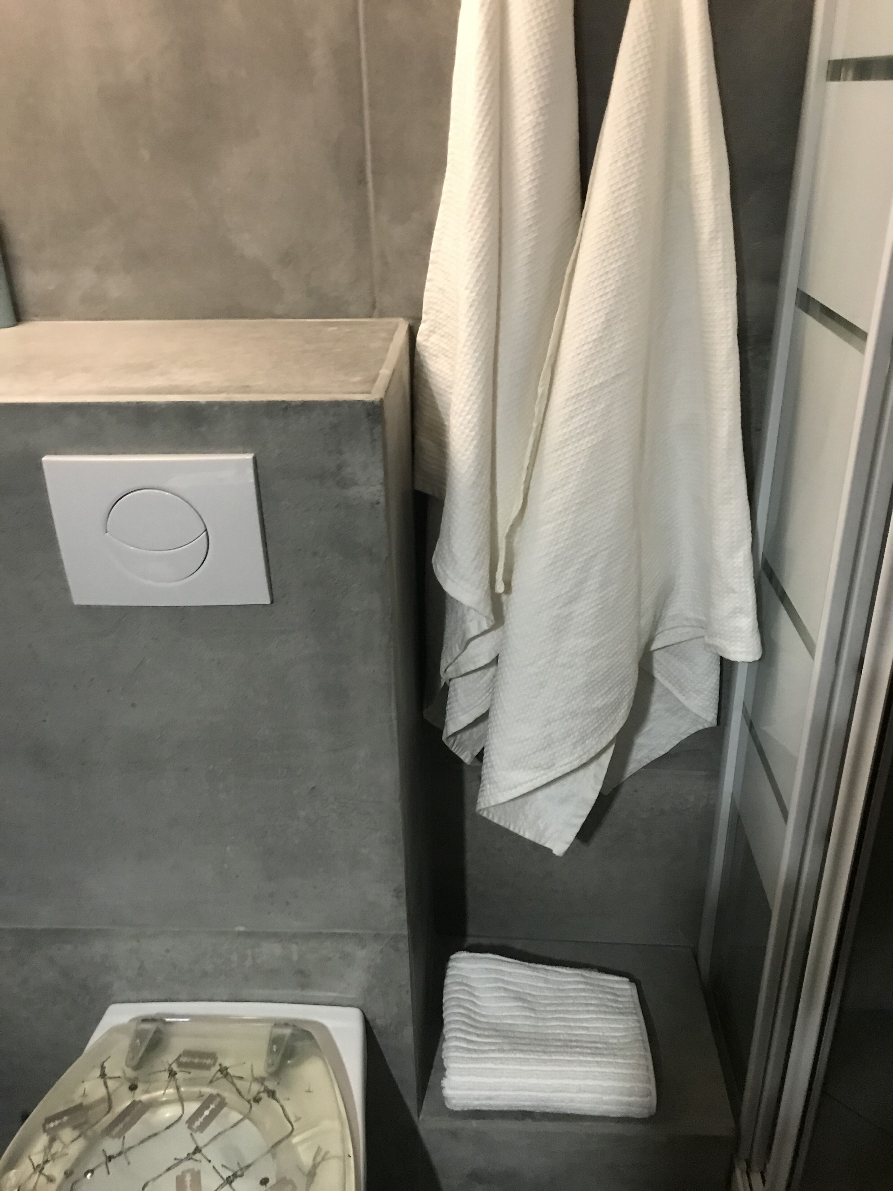 Un baño con inodoro, un perchero con dos toallas y una pila de toallas dobladas en el suelo.