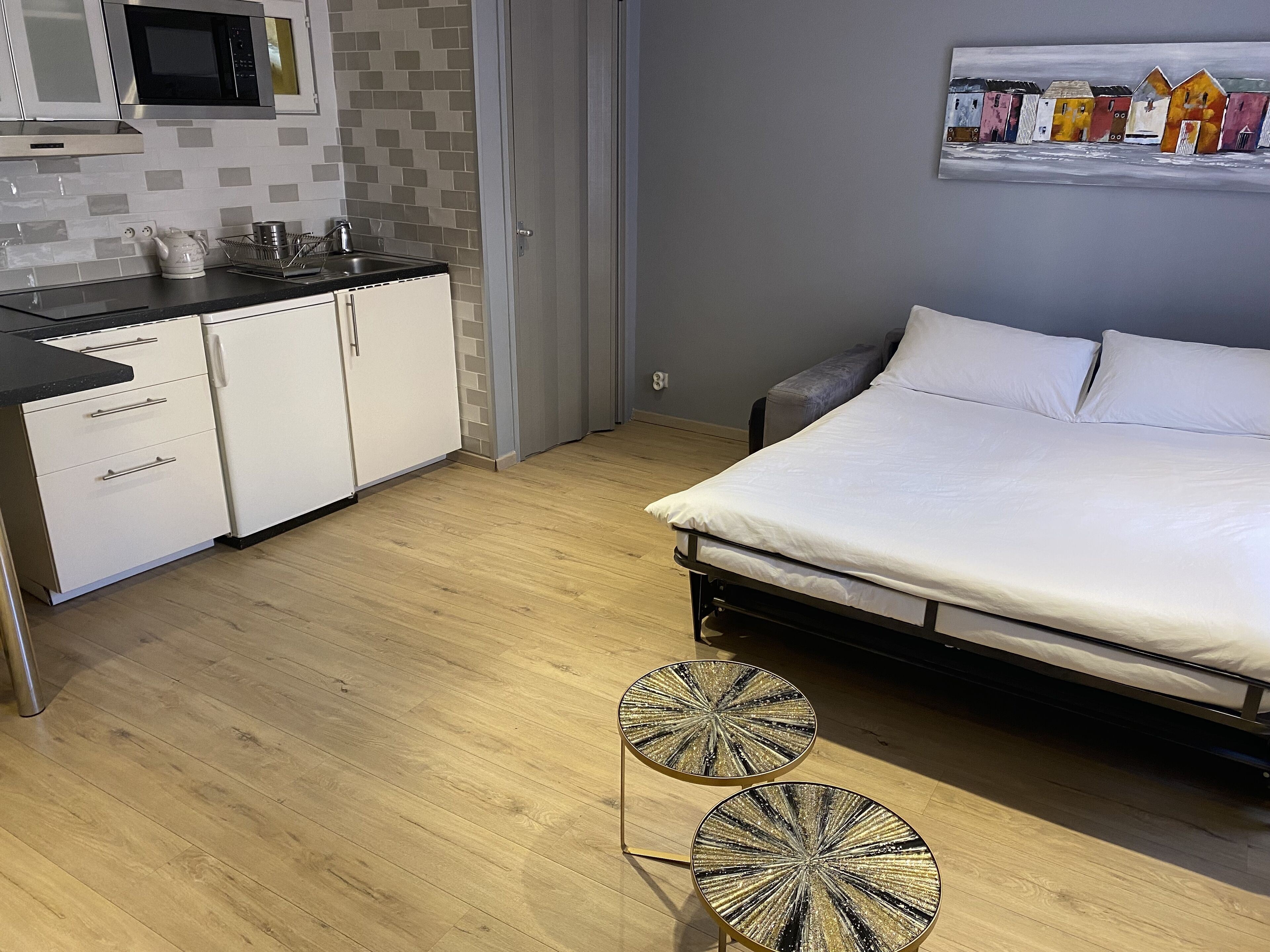 A compact bedroom with a bed, a small kitchenette, and two round side tables.