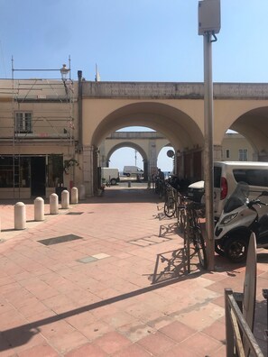 A paved pedestrian area with a series of arches, a white van, and bicycles parked.