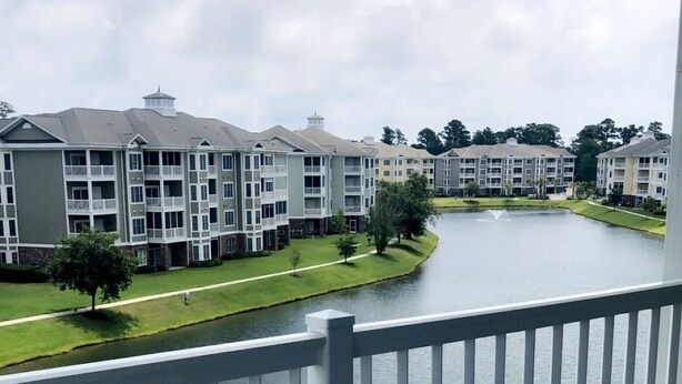 A balcony with a glass table and blue chairs, overlooking a body of water and a row of buildings. - Amazing Clean 4th floor condo, newly furnished, new paint,carpet,privet  Wifi,  (Myrtle Beach)