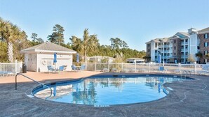 A swimming pool with lounge chairs and a small building, surrounded by a fence and trees. - Amazing Clean 4th floor condo, newly furnished, new paint,carpet,privet  Wifi,  (Myrtle Beach)