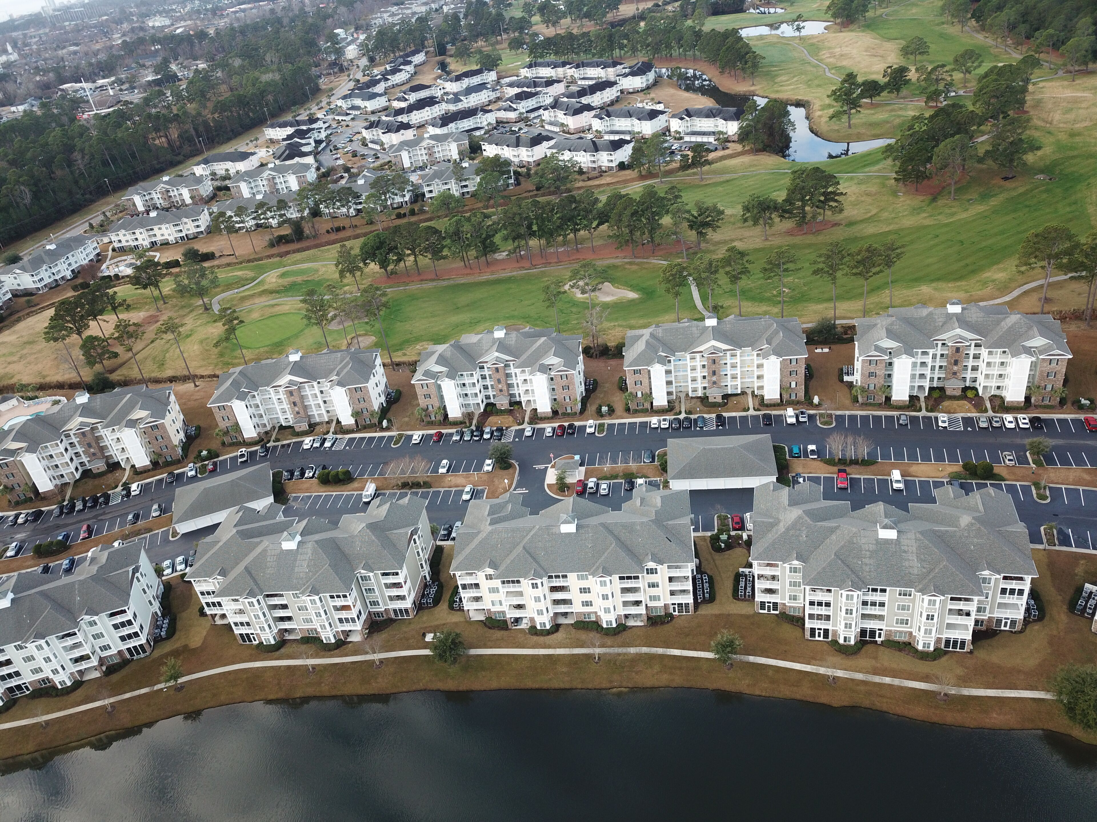 Vue aérienne d’un quartier résidentiel comprenant plusieurs immeubles d’appartements, un parking et une étendue d’eau.