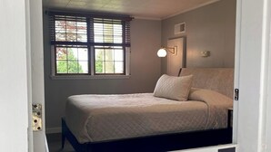 A bedroom with a bed, a window with blinds, a wall-mounted light fixture, and a door with a number '4' on the wall. - 1-bedroom guestroom in a lodge, 9 miles from Cedar Point (Sandusky)