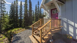 A wooden staircase leading to a house with a red door, surrounded by tall trees and a gravel path. - Alpenglow Ridge Fireweed (Healy)