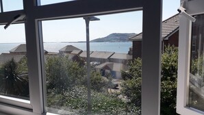 Vista pela janela de uma área residencial com casas, um corpo d'água e uma colina distante.