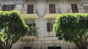 A multi-story building with balconies, large windows, and lush green trees in front. - Sammartino suite (Palermo)
