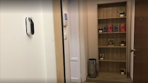A hallway with a door on the left, a digital lock, a small trash bin, and a wooden shelf with decorative items. - Sammartino suite (Palermo)