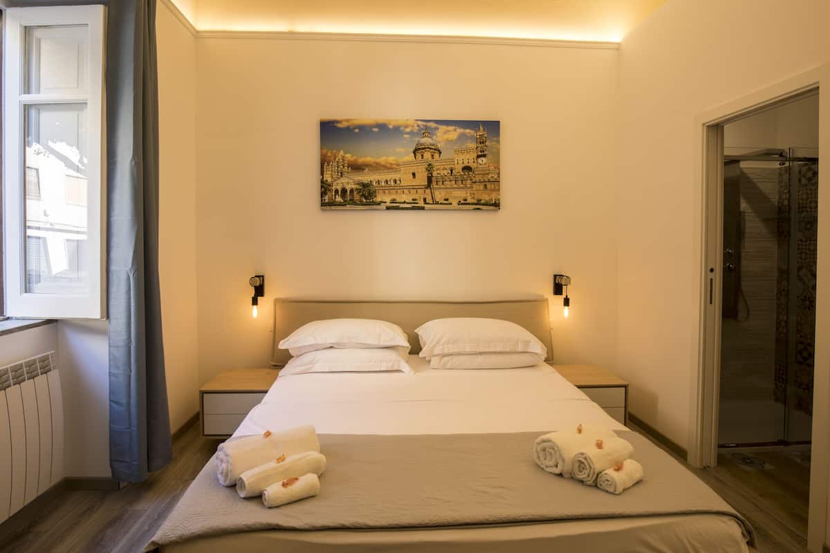 Ein Hotelzimmer mit einem Bett, zwei Nachttischen, einem Wandbild, einem Fenster mit Vorhängen und einer Dusche.