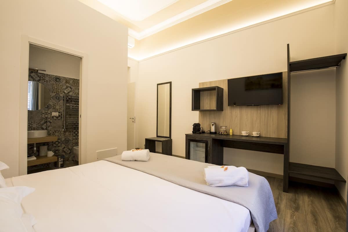 Ein Hotelzimmer mit Bett, Bad, Fernseher und Schreibtisch mit Spiegel.
