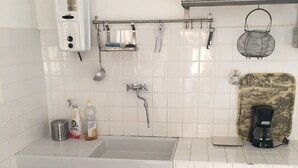 A kitchen with white cabinets, a sink, a coffee machine, and a shelf with a kettle and a yellow pot. - village house Ota (Ota)