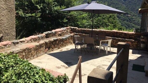 An outdoor patio with stone walls, a table with chairs, and an umbrella. - village house Ota (Ota)