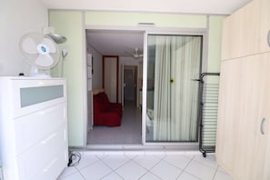 A room with a sliding glass door leading to a hallway, a white dresser with drawers, a standing fan, and a red chair.