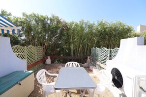 A patio with a table and chairs, a white Bosch fan, and a green fence.