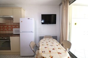A compact kitchen with a refrigerator, microwave, oven, and a flat-screen TV mounted on the wall.