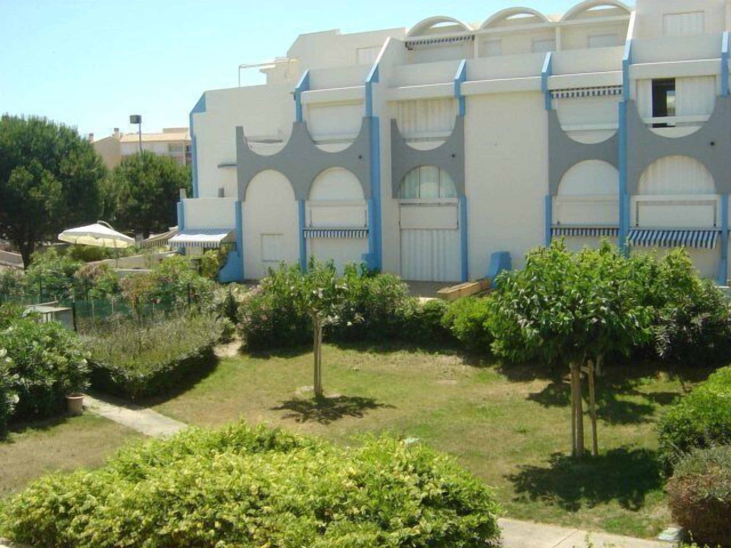 A building with multiple balconies and a well-maintained garden with trees and shrubs.