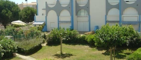 A building with multiple balconies and a well-maintained garden with trees and shrubs.
