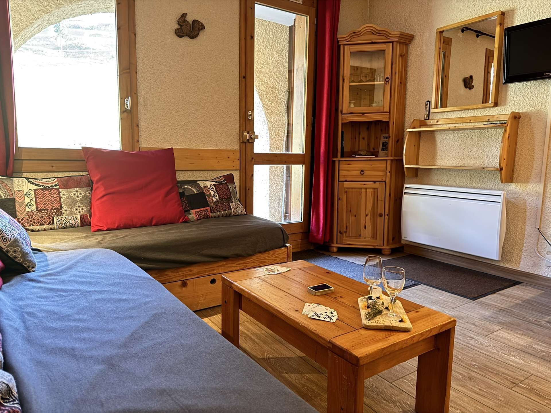 Ein gemütliches Zimmer mit einer Couch, einem Holzschrank, einem Fernseher und einem kleinen Tisch mit Gläsern und einer Spielkarte.