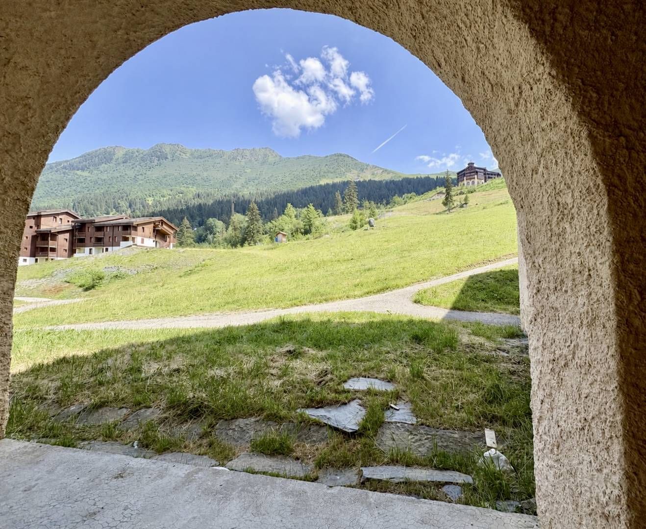 Une vue à travers une arche d’un bâtiment, avec un champ verdoyant et des montagnes en arrière-plan.