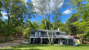 A two-story house with a porch, surrounded by a well-maintained lawn and trees. - Beautiful lake side lower unit cabin on pelican lake (Pequot lakes)