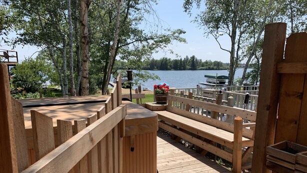 A wooden deck with a bench and a planter with flowers, overlooking a lake. - Beautiful lake side lower unit cabin on pelican lake (Pequot lakes)