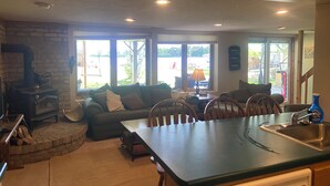 A cozy kitchen with a stone fireplace, a dining area with a table and chairs, and large windows offering a view of the outdoors. - Beautiful lake side lower unit cabin on pelican lake (Pequot lakes)