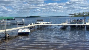 A marina with boats docked, a sandy shore, and a distant island. - Beautiful lake side lower unit cabin on pelican lake (Pequot lakes)