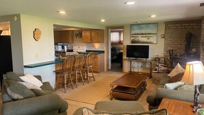 A cozy living room with green sofas, a wooden coffee table, and a TV. There's a kitchen with wooden cabinets and a stove, and a fireplace with a TV. - Beautiful lake side lower unit cabin on pelican lake (Pequot lakes)