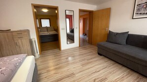 A room with a wooden floor, a grey sofa, a bed with a floral bedspread, a wooden wardrobe, and a mirror on the wall. - Non-smoking vacation apartment 50sqm, no. 1, 2 bedrooms, max. 4 persons - (Rust)