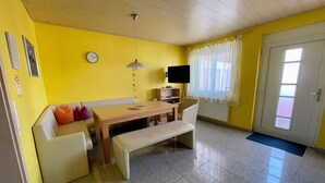 A room with a wooden table, a bench, a sofa, a television, and a door with a window. - Non-smoking vacation apartment 50sqm, no. 1, 2 bedrooms, max. 4 persons - (Rust)